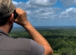man with binoculars looking out on forest canopy 
